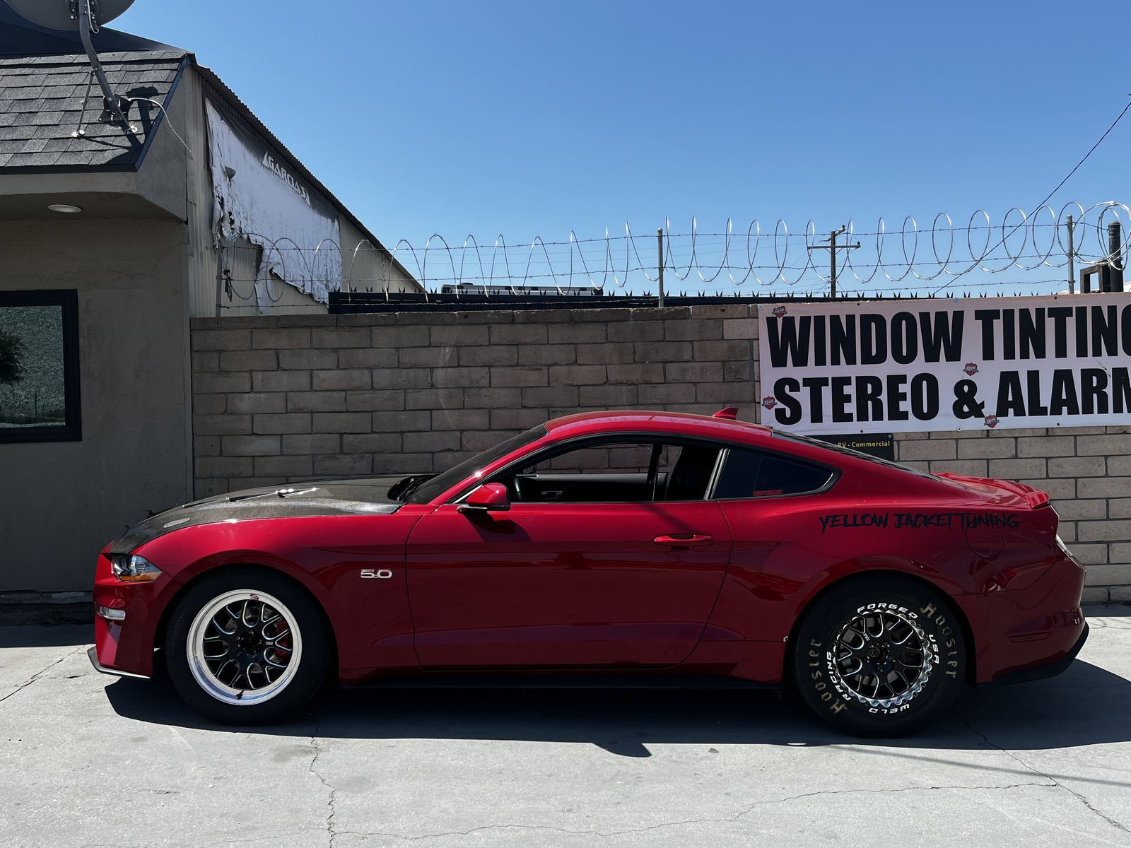 Red Ford Mustang 5.0 with aftermarket black wheels parked outside the shop